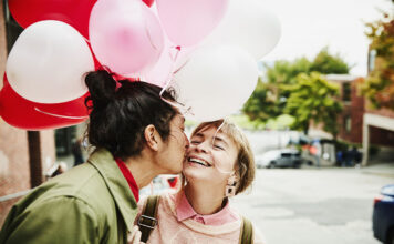 Man Kissing Smiling Girlfriend On Cheek While Giving Her Balloons During Date on Valentines day