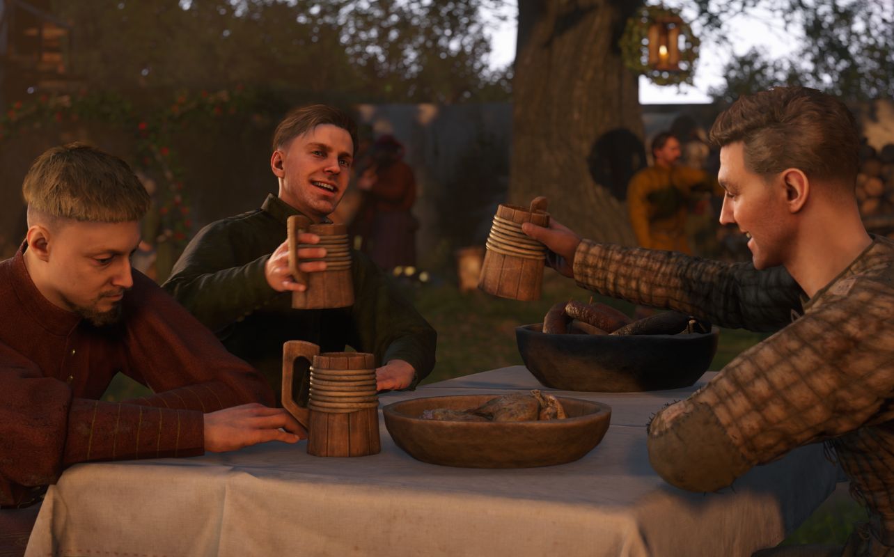 A screenshot of the video game Kingdom Come Deliverance II depicts three men sitting at a table, smiling as they clink together pints of ale.