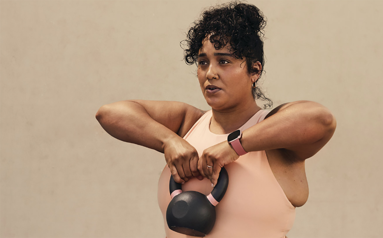 Women lifting a kettlebell wearing the Fitbit Versa 4