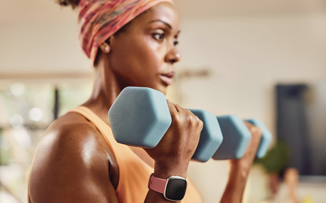 A woman lifting weights wearing the Fitbit Versa 4