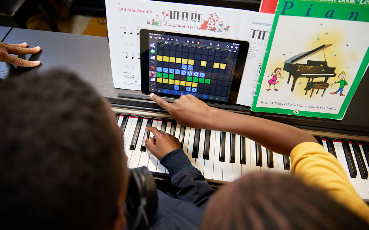 Children creating music through an iPad with a piano.