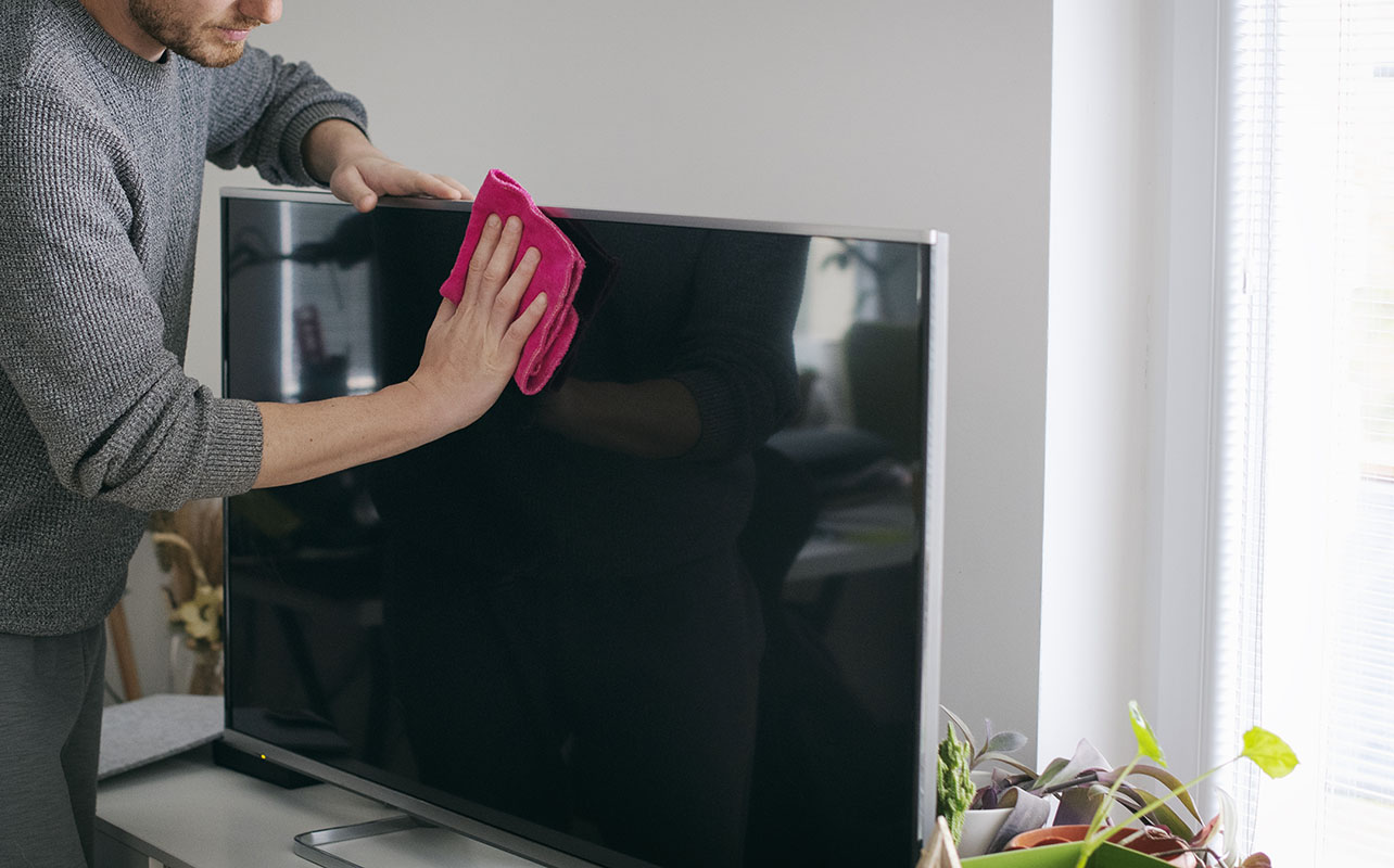 Close up of man cleaning a TV screen with a microfibre cloth. 