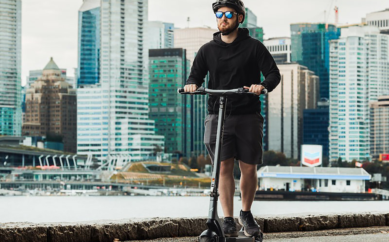 A man rising the Apollo City electric scooter by the water and smiling.