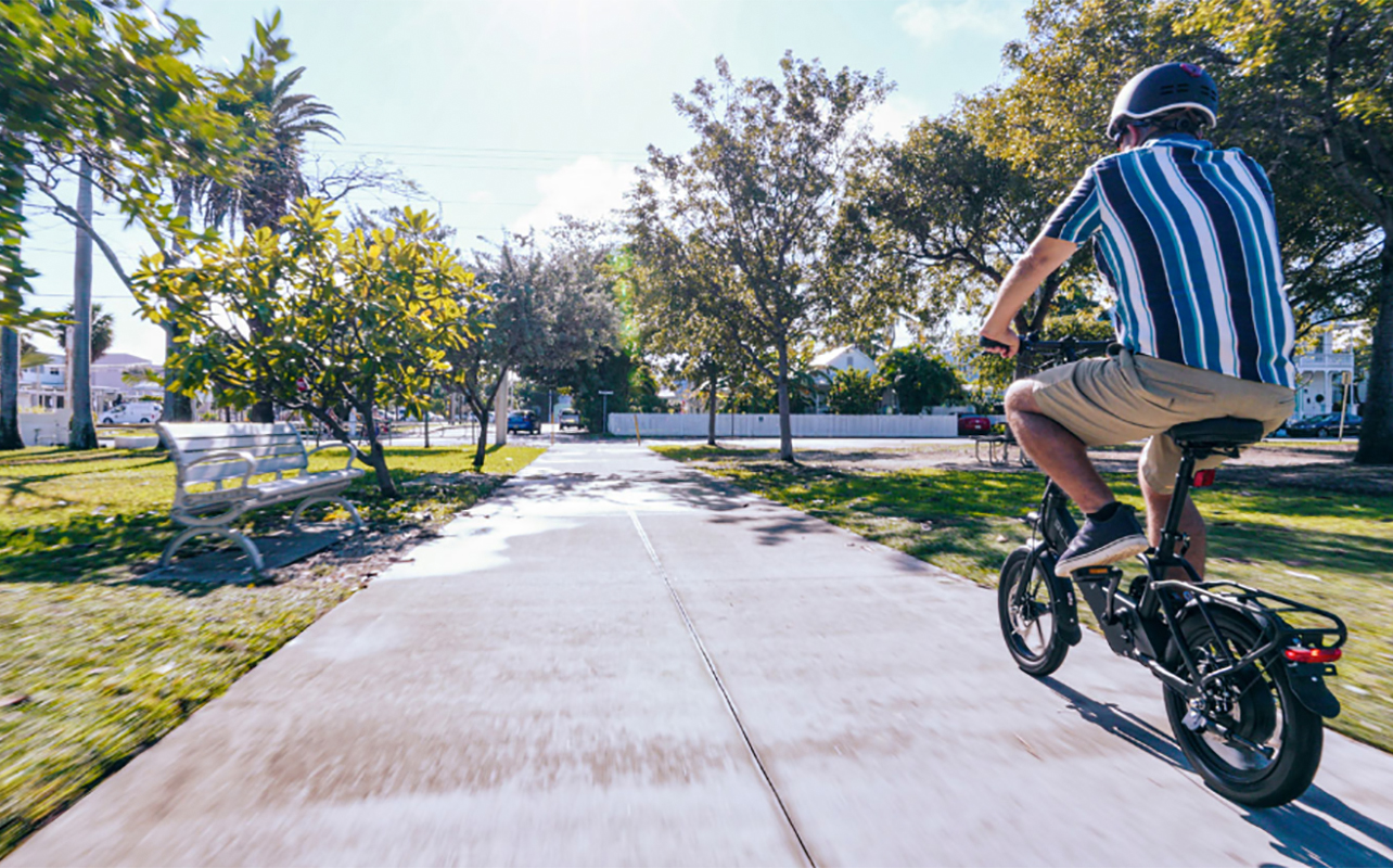 View of a man riding a Blutron e-bike down a road from behind.