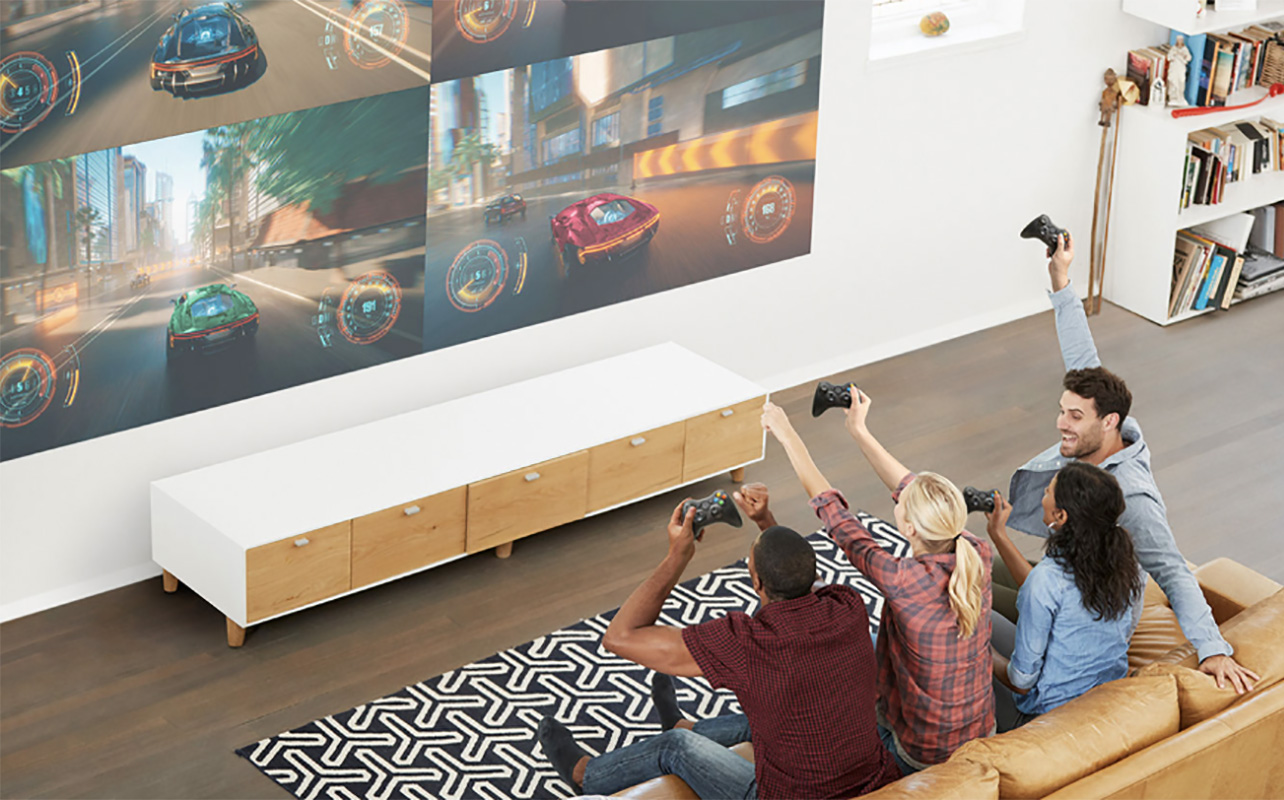 An overhead view of four people cheering while playing a video game on a large screen with an Epson projector.