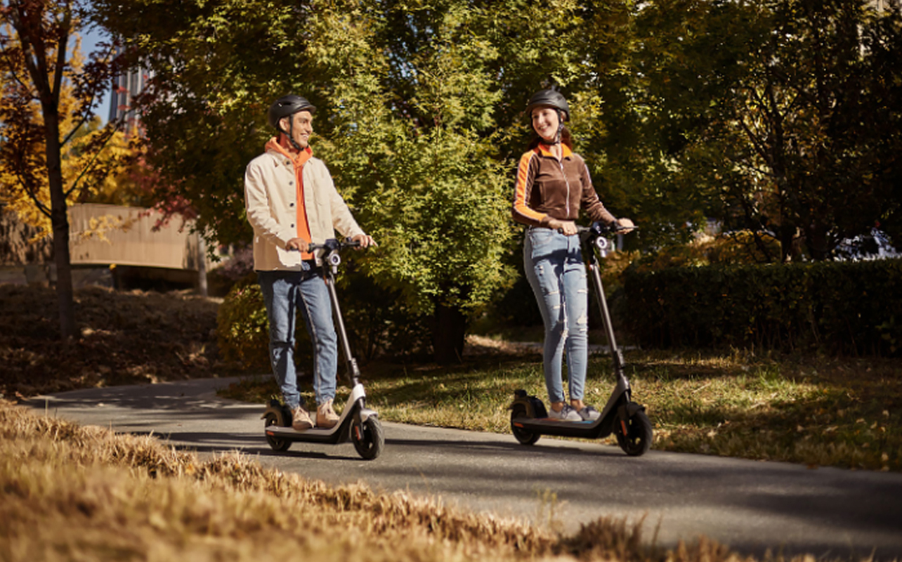 Two people riding electric scooters side by side on a trail.