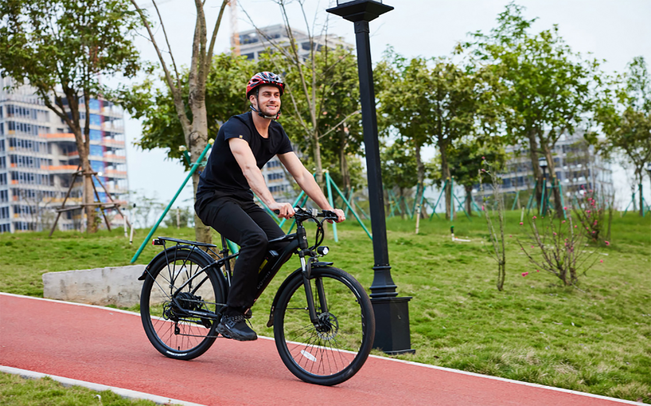 Un homme qui fait du vélo électrique GoPowerBike sur un sentier près d'un parc et qui sourit. 