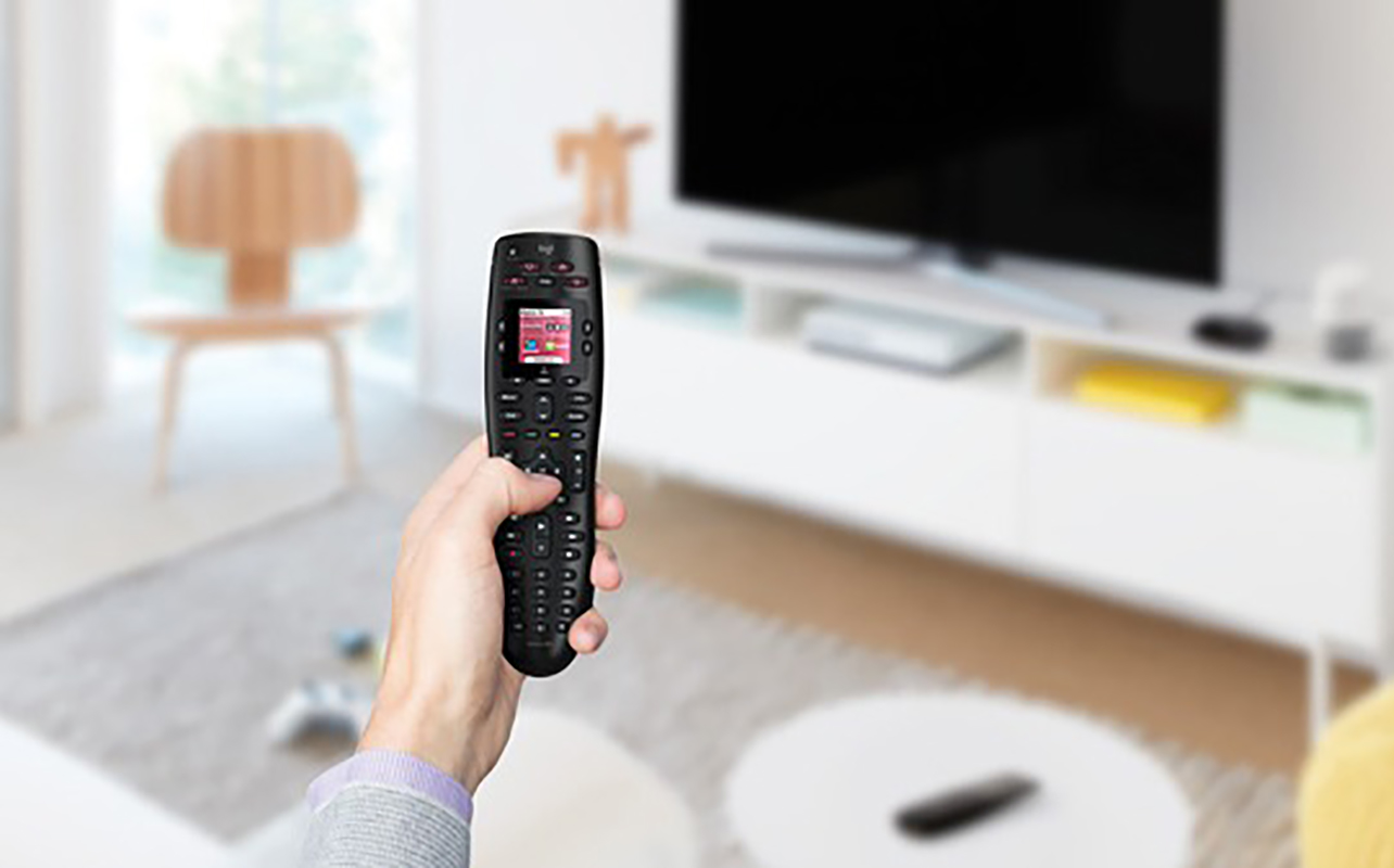 A hand holding a Harmony 665 universal remote in front of a TV