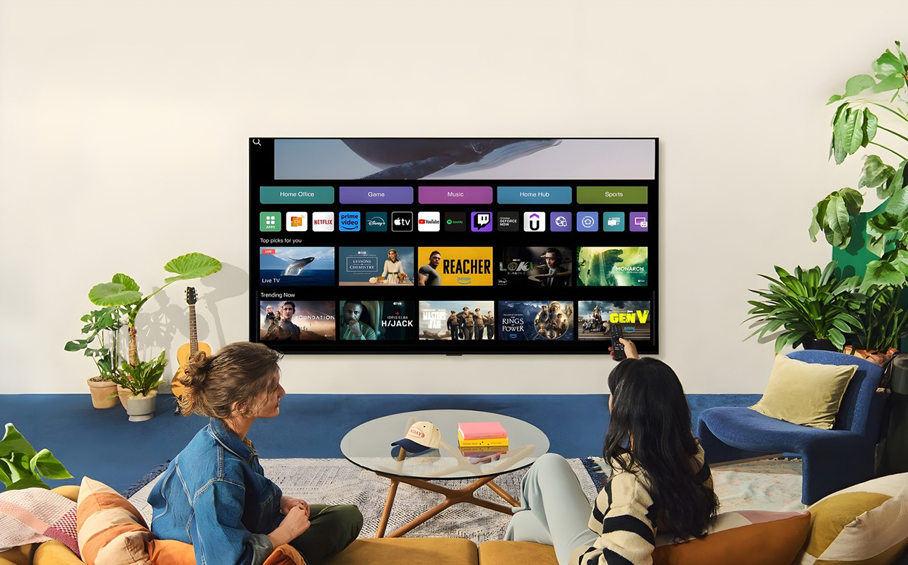 Two women watching an LG TV in a living room with one holding a remote.