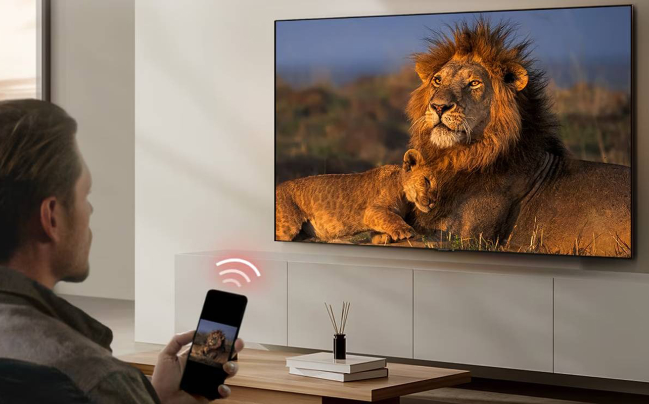 A man holding a remote up to a Google TV with the Wi-Fi symbol coming from it to show casting.