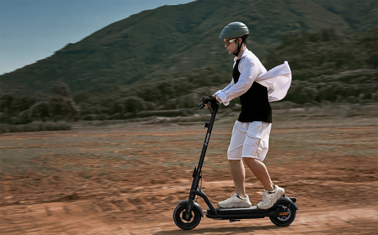 A man riding a Navee e-scooter down a bumpy rode, his white shirt blowing in the wind behind him.