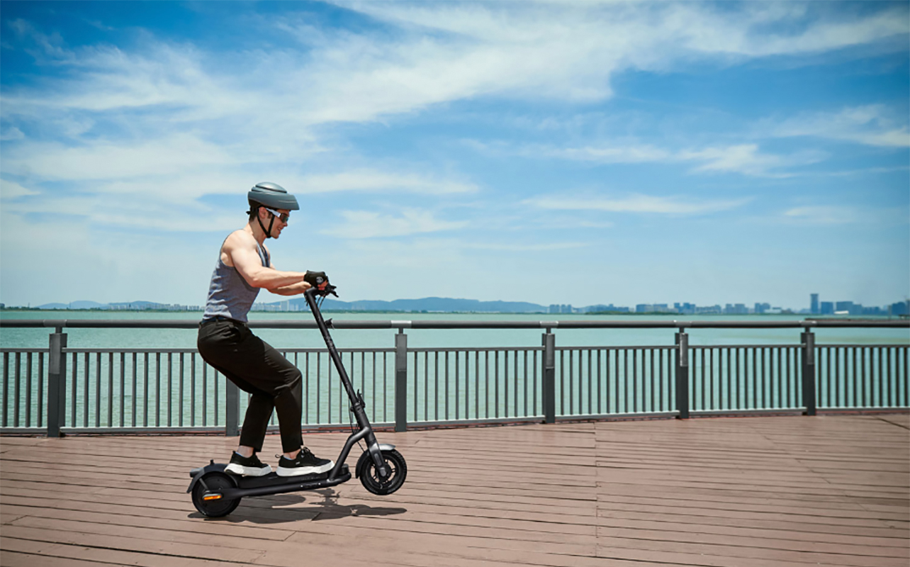 A man  riding a Navee electric scooter by the water