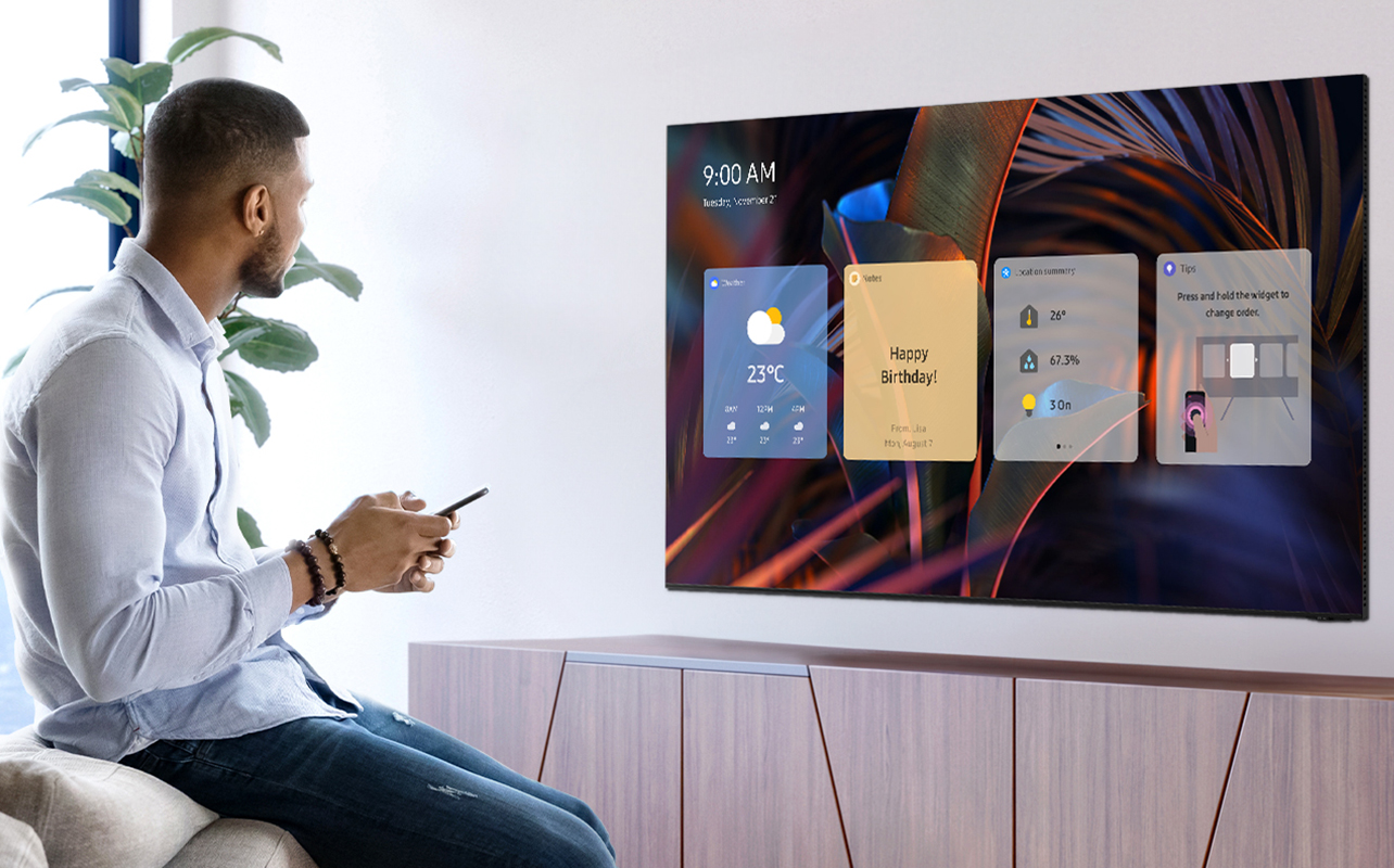 A man sitting behind the sofa holds the remote on the Samsung Old TV that displays the menu.