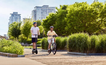 Two people riding a Segway Ninebot e-bike and e-scooter down a sunny road.