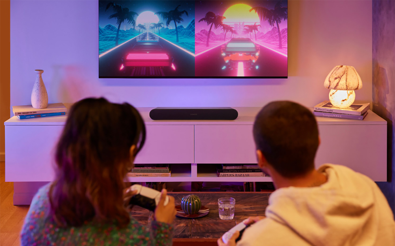 A couple playing video games on the couch with a TV and Sonos Ray sound bar in front of them.