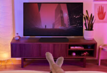 A Sonos Ray sound bar beneath a TV with feet relaxing on the table in view in front of it.