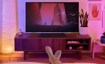 A Sonos Ray sound bar beneath a TV with feet relaxing on the table in view in front of it.