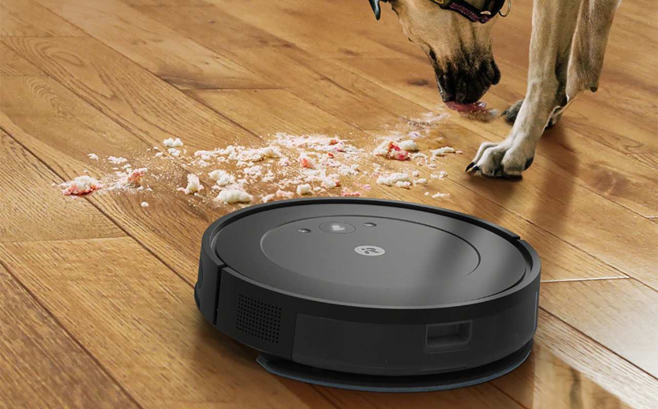 An iRobot Roomba Combo Essential picking up a mess, a dog visible in the corner.