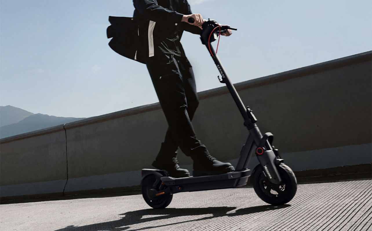 A man's legs riding a Segway Ninebot Max G3 electric scooter.