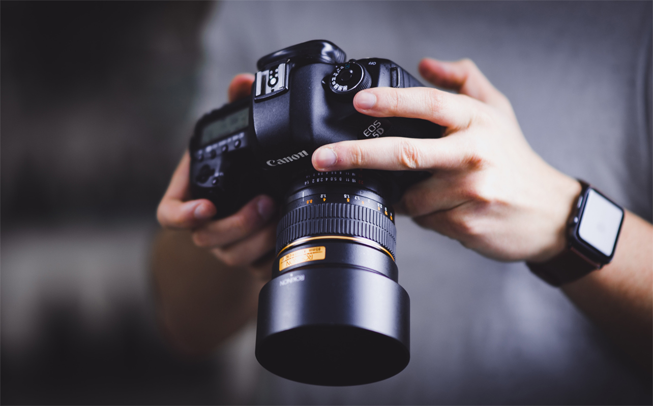 Homme tenant un appareil photo Canon avec un objectif standard.