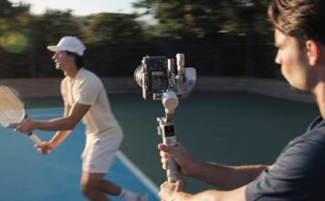 Man using camera on gimbal to track tennis player.