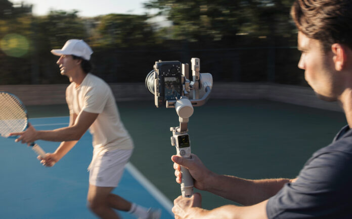Man using camera on gimbal to track tennis player.