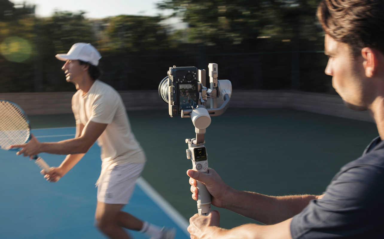 Man using camera on gimbal to track tennis player.