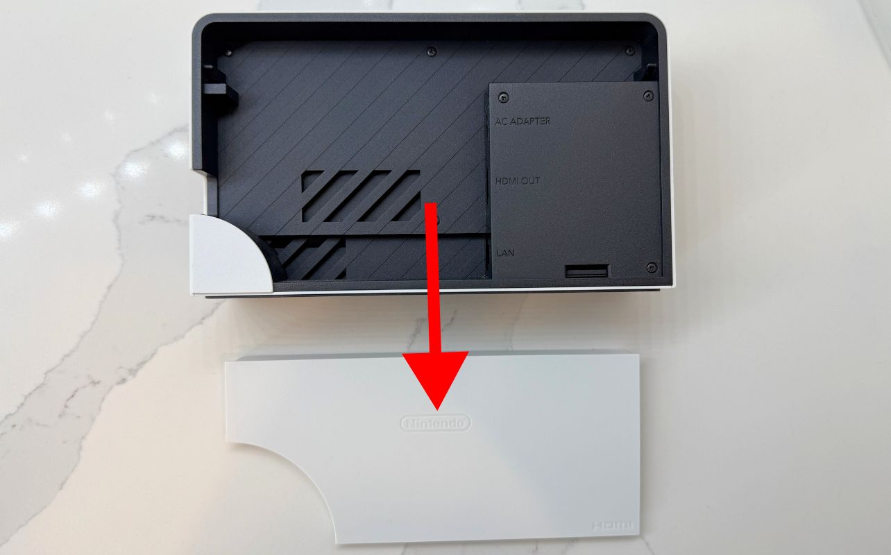 The Nintendo Switch dock back panel removed with a red arrow indicating the direction the white panel needs to be moved to be removed.