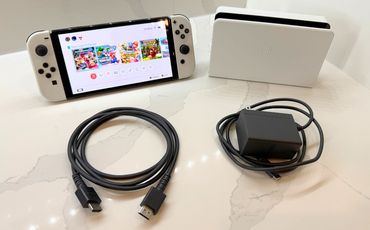 Nintendo Switch OLED console on a marble surface with the dock, HDMI cable and AC power adaptor.