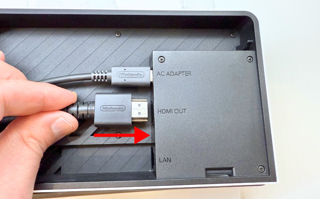 The Nintendo Switch dock back panel removed with a red arrow indicating where the HDMI cable should be plugged in.