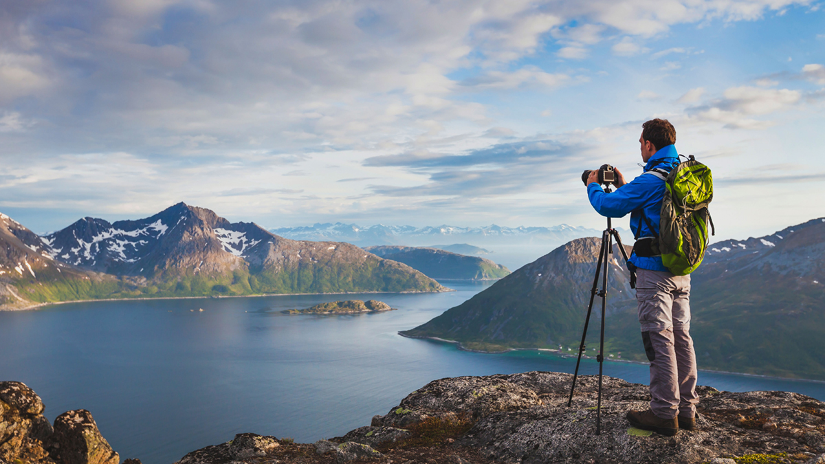 Man capturing wide vista with wide-angle lens on tripod.