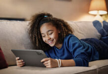 A young girl lying on the couch smiling while holding a Lenovo Tab M11 tablet.