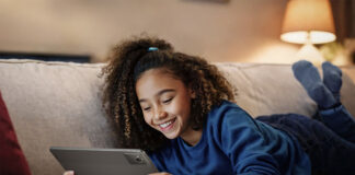 A young girl lying on the couch smiling while holding a Lenovo Tab M11 tablet.