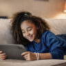 A young girl lying on the couch smiling while holding a Lenovo Tab M11 tablet.