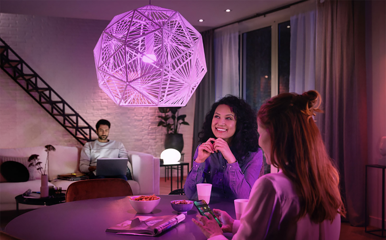 Deux femmes assises dans une cuisine, un homme sur un portable en arrière-plan avec des lumières Hue de Philips.
