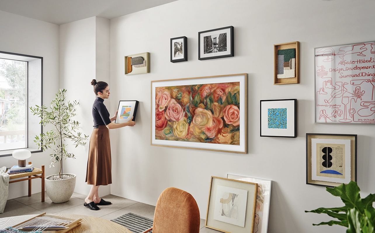 A woman arranging Samsung Music Frame around a mounted Samsung The Frame TV.