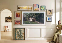 A Samsung The Frame TV mounted on the wall with smaller picture frames around it, a woman sitting on the windowsill to the right.