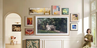 A Samsung The Frame TV mounted on the wall with smaller picture frames around it, a woman sitting on the windowsill to the right.