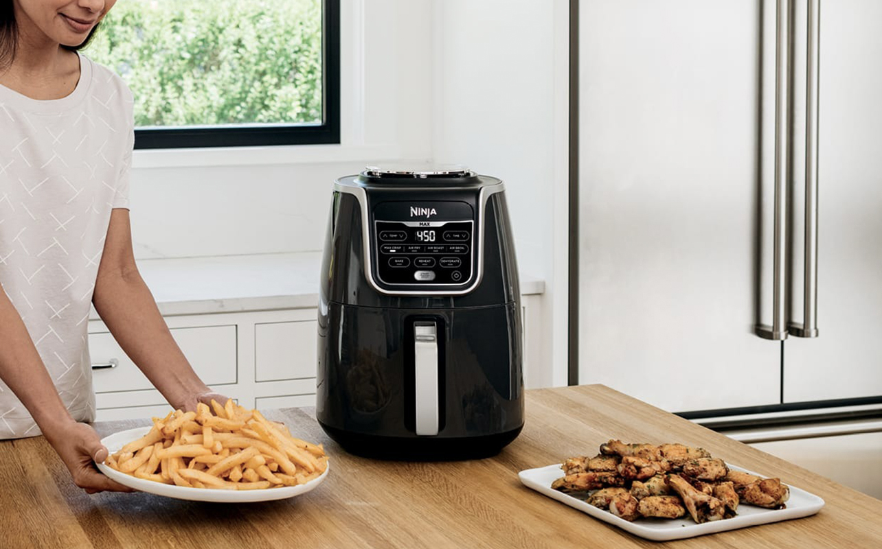 A woman with the Ninja Max XL air fryer and a plate of fries and chicken wings