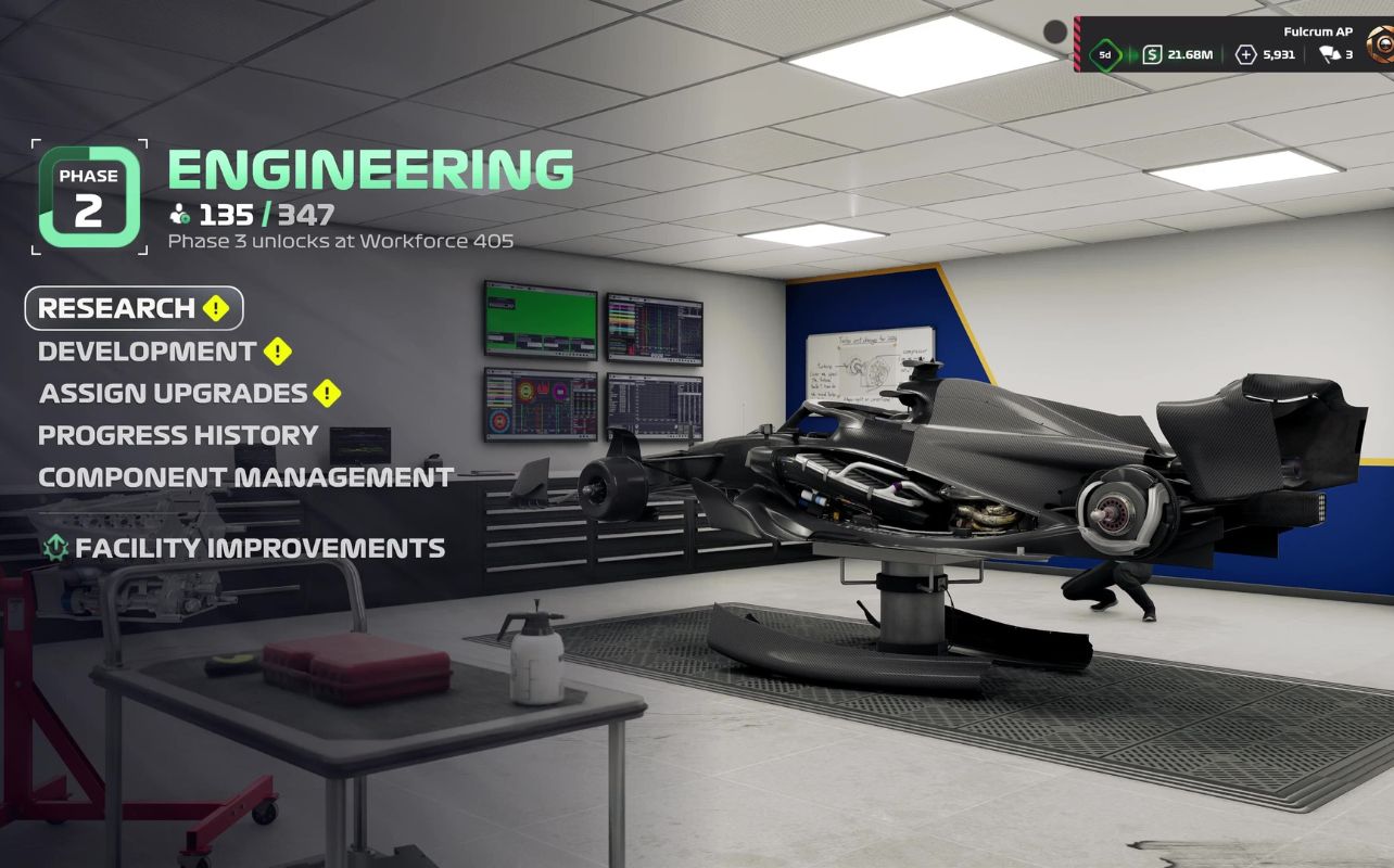 Une capture d'écran du mode Mon écurie de F1 25, représentant l'atelier d'ingénierie avec une voiture de Formule 1 soulevée par un pont élévateur hydraulique. La scène met en valeur les graphismes améliorés du jeu, notamment l'équipement détaillé du garage, l'éclairage réaliste et un espace de travail bien éclairé. Les composants complexes de la voiture sont également visibles.