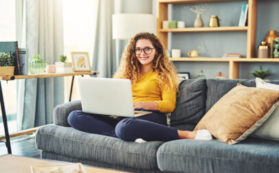 Woman sitting on a couch with a laptop on her lap.