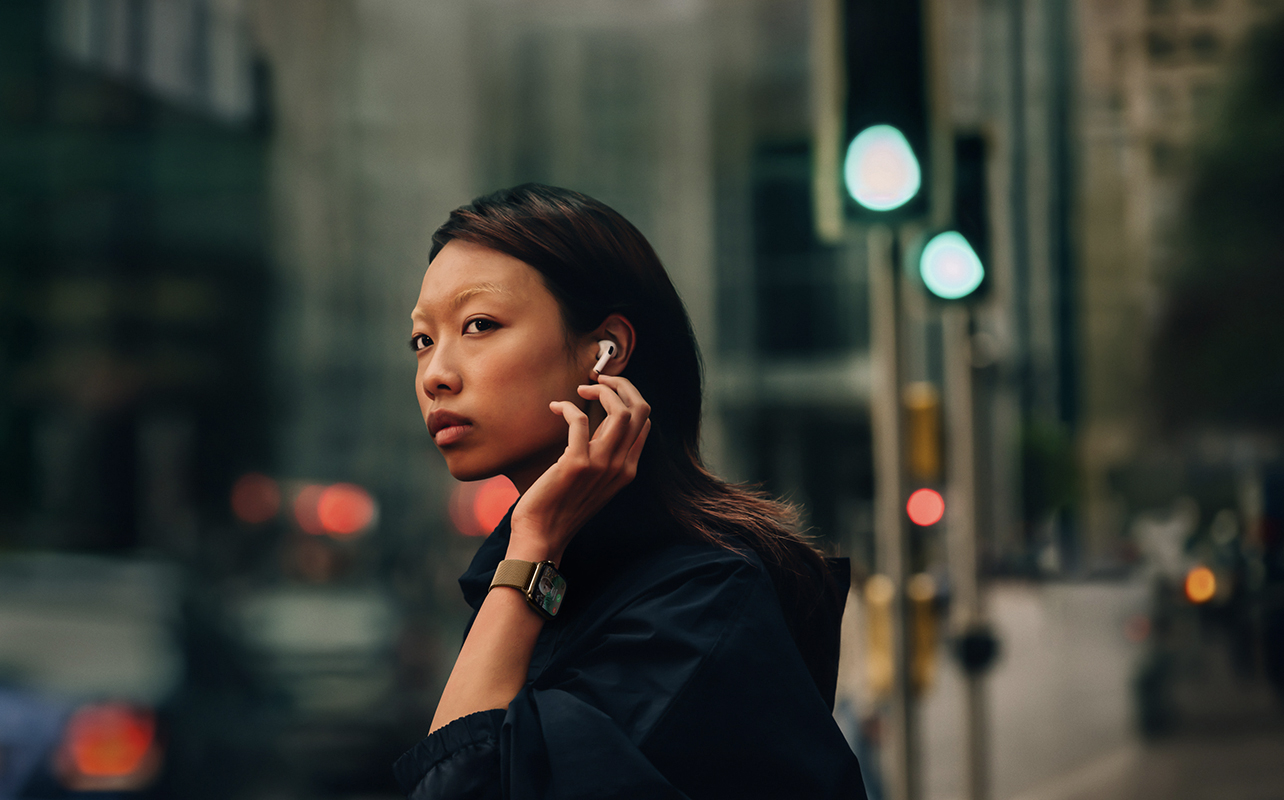 A woman walking down the street wearing an Apple Watch and Appel AirPods.