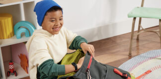 A young boy packing his schoolbag while wearing the Fitbit Ace 3 smartwatch.