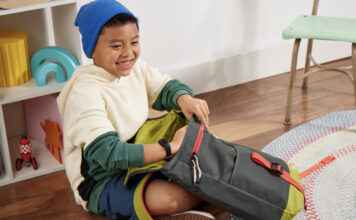A young boy packing his schoolbag while wearing the Fitbit Ace 3 smartwatch.