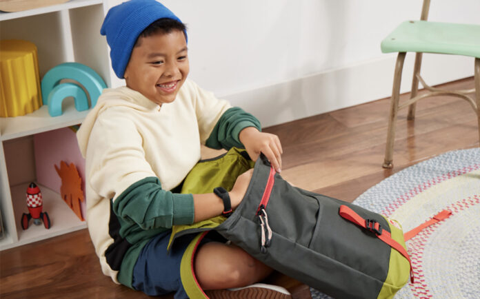 A young boy packing his schoolbag while wearing the Fitbit Ace 3 smartwatch.