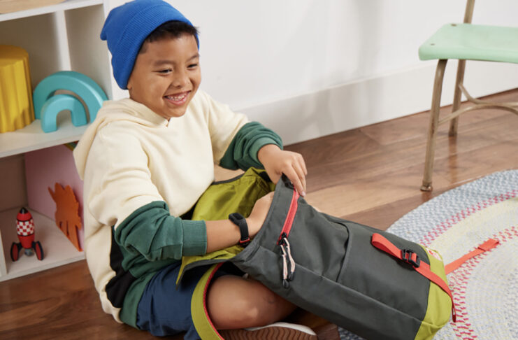 A young boy packing his schoolbag while wearing the Fitbit Ace 3 smartwatch.