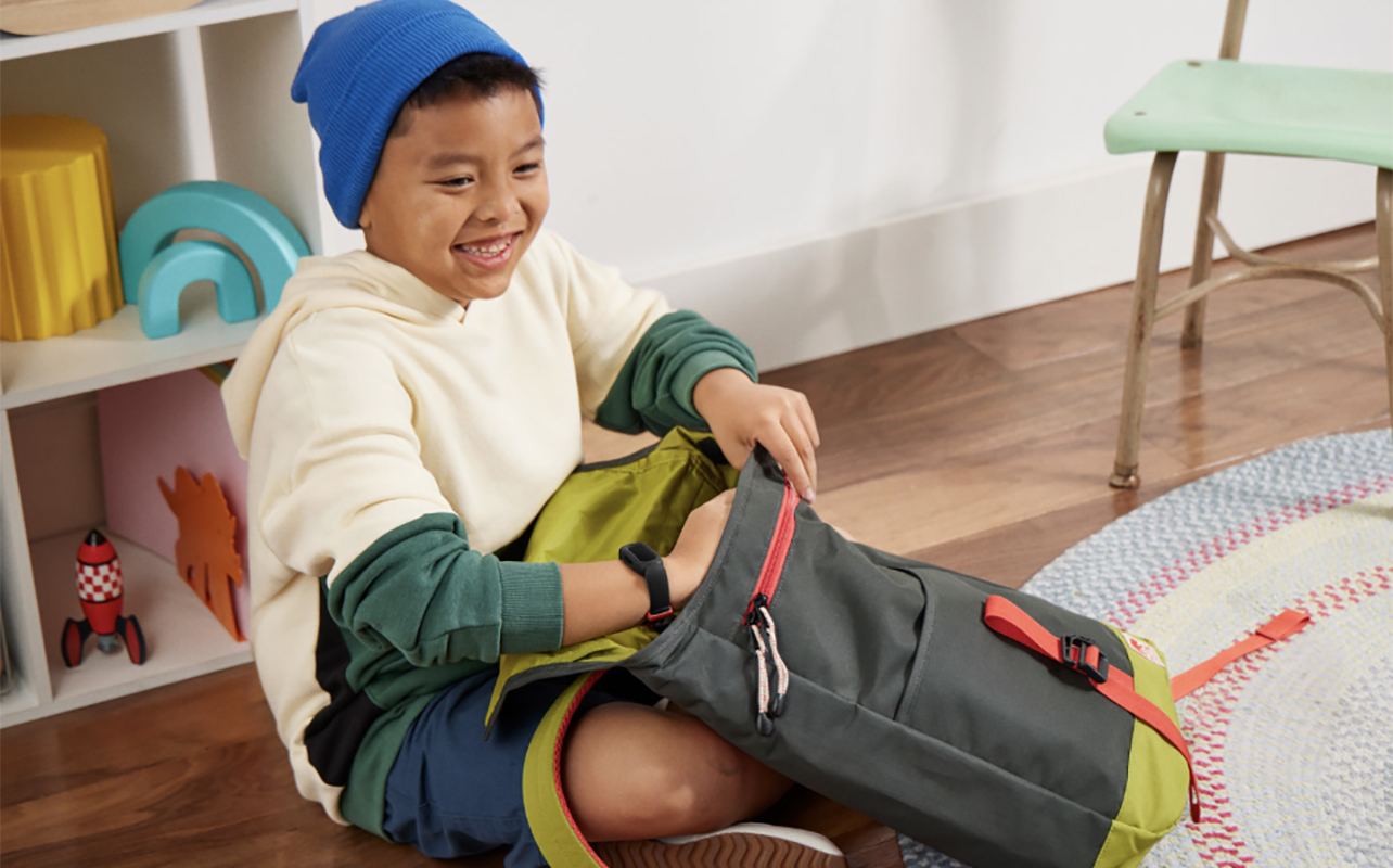 A young boy packing his schoolbag while wearing the Fitbit Ace 3 smartwatch.
