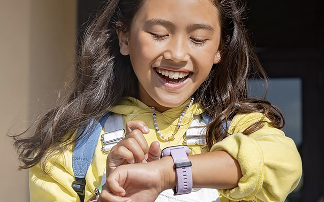 A girl smiling while looking at a Garmin Bounce smartwatch on her wrist.