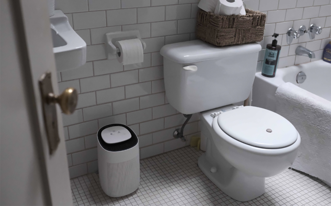 The JS Vanguard 2.0 air purifier and dehumidifier in a bathroom beside a toilet.