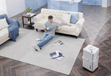 An overhead view of a man sitting on a living room floor with a Midea Cube dehumidifier in the bottom, right corner.